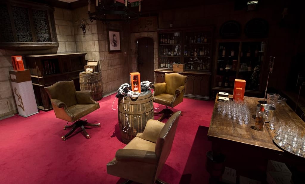 Experiential event room - plush red carpet, leather chairs, fireplace and whiskey glasses laid out with VR headsets