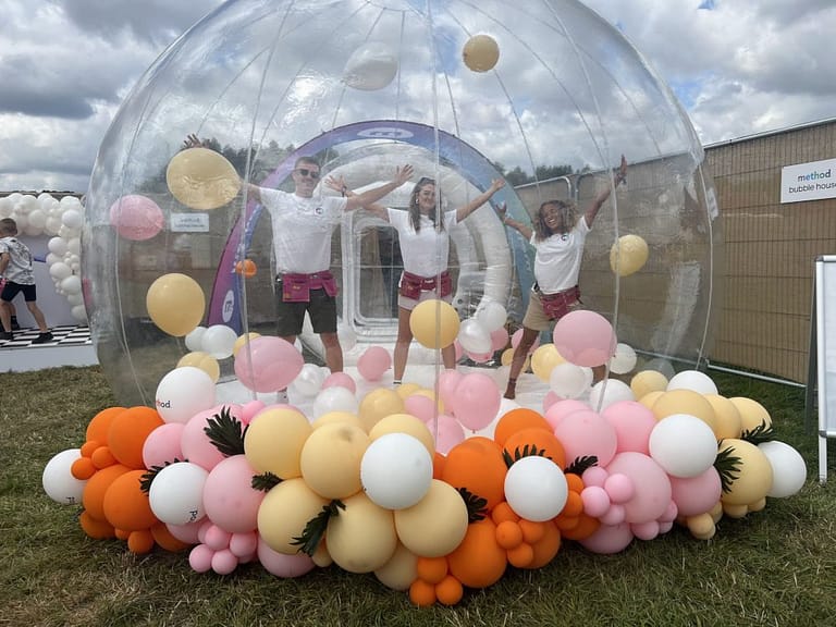 People in a see-through plastic dome surrounded by pink yellow and white balloons